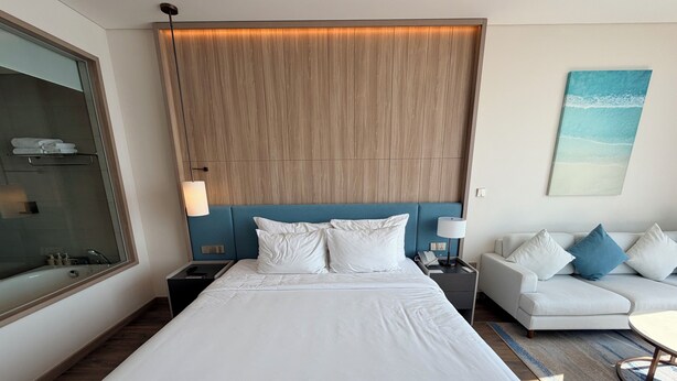 Una habitación de hotel moderna con una cama grande, una mesita de noche, un sofá y un cuadro en la pared.
