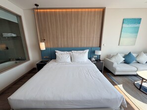 A modern hotel room with a large bed, a nightstand, a bedside table, a sofa, and a painting on the wall. - Bao Chau Hotel (Bai Chay)