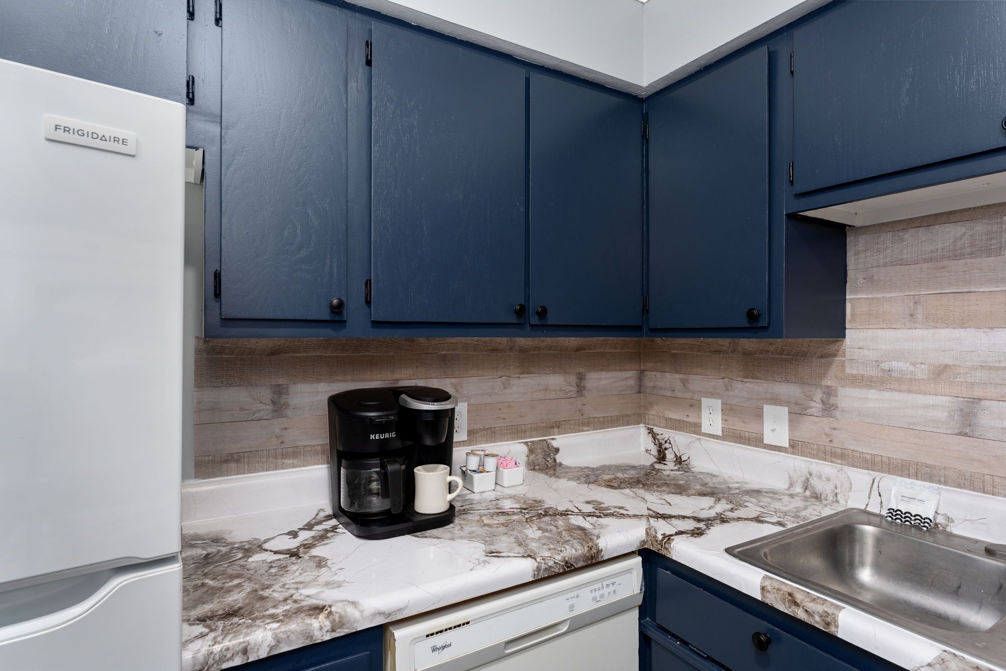 A kitchen with dark blue cabinets, a white refrigerator, a coffee maker, and a dishwasher.
