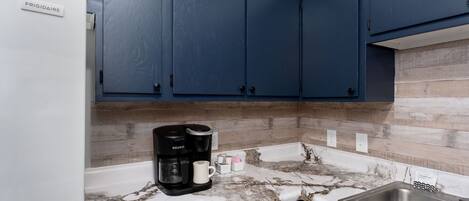 A kitchen with dark blue cabinets, a white refrigerator, a coffee maker, and a dishwasher.