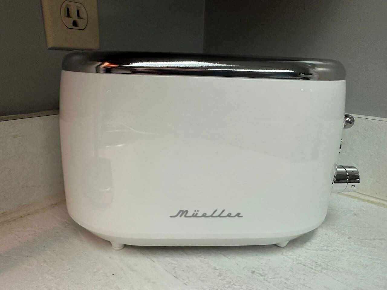 Uma torradeira branca com a marca 'Müller' em cima de uma bancada.