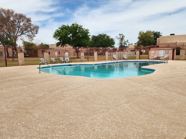 A swimming pool with a curved edge, surrounded by a brick wall and metal fencing. There are lounge chairs and a sign indicating no diving is allowed.
