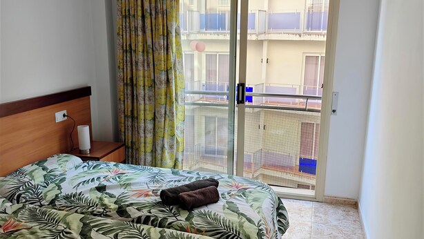 A hotel room with a bed, a nightstand, a window with curtains, and a view of a balcony. - Apartment Seawolf, Lloret de Mar (Lloret de Mar)