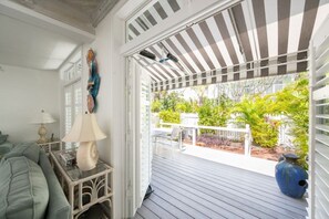 Een overdekte veranda met uitzicht op een tuin, een witte balustrade en een blauwe vaas.