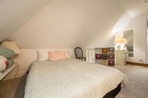Een slaapkamer met een bed, een stoel, een nachtkastje, een lamp en opbergmeubels.