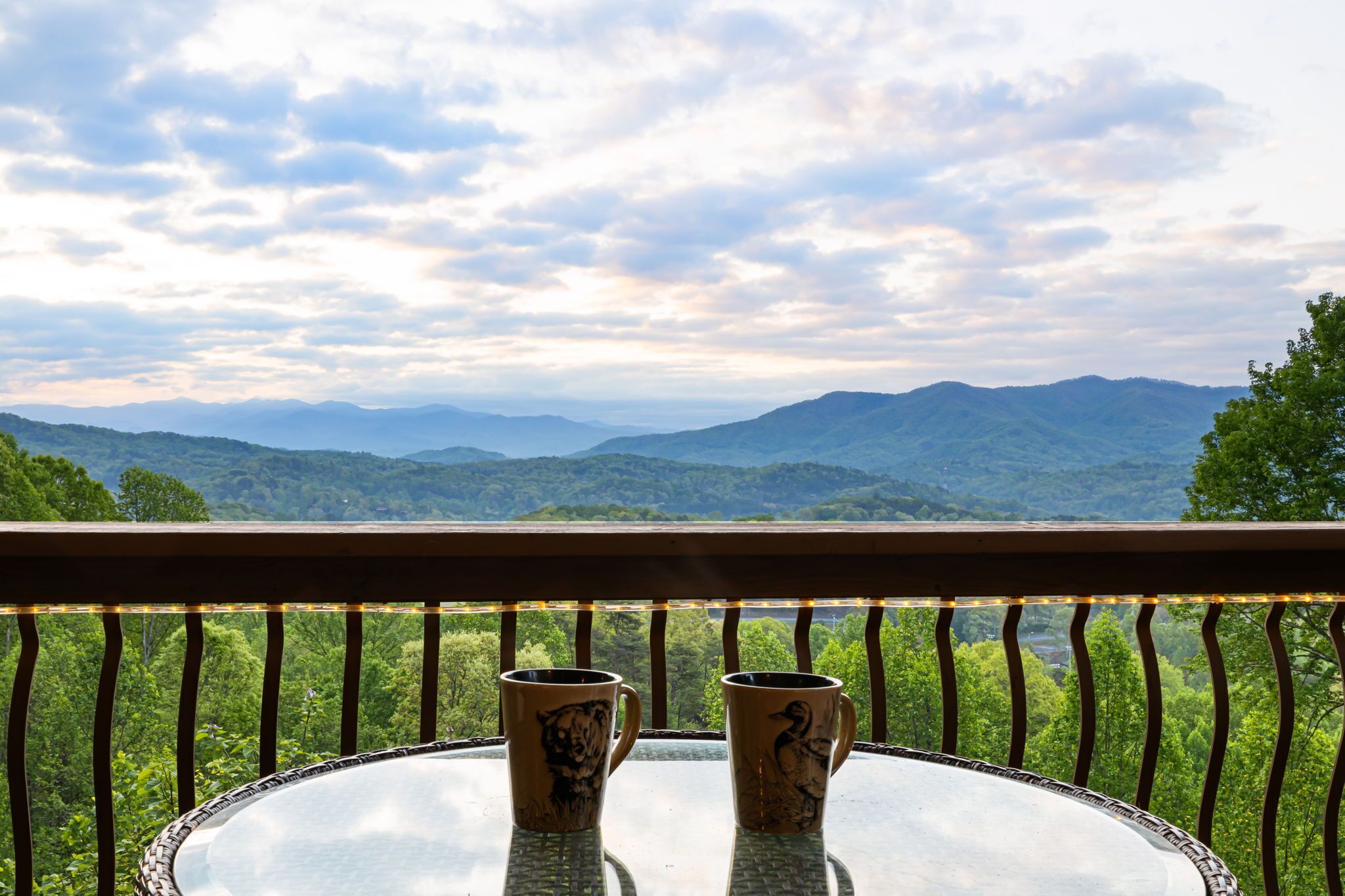 A table with two mugs on a balcony overlooking a mountainous landscape.