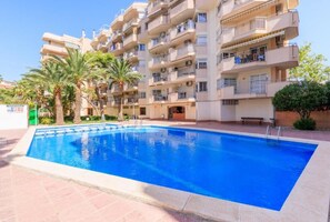 Une piscine entourée d’un immeuble à plusieurs étages doté de balcons, de palmiers et surplombant un ciel dégagé.