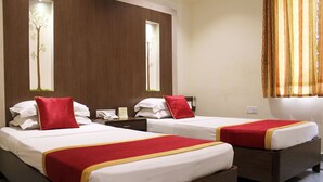 Quarto de hotel com duas camas de solteiro, cada uma com colcha vermelha e branca, e cabeceira de madeira.