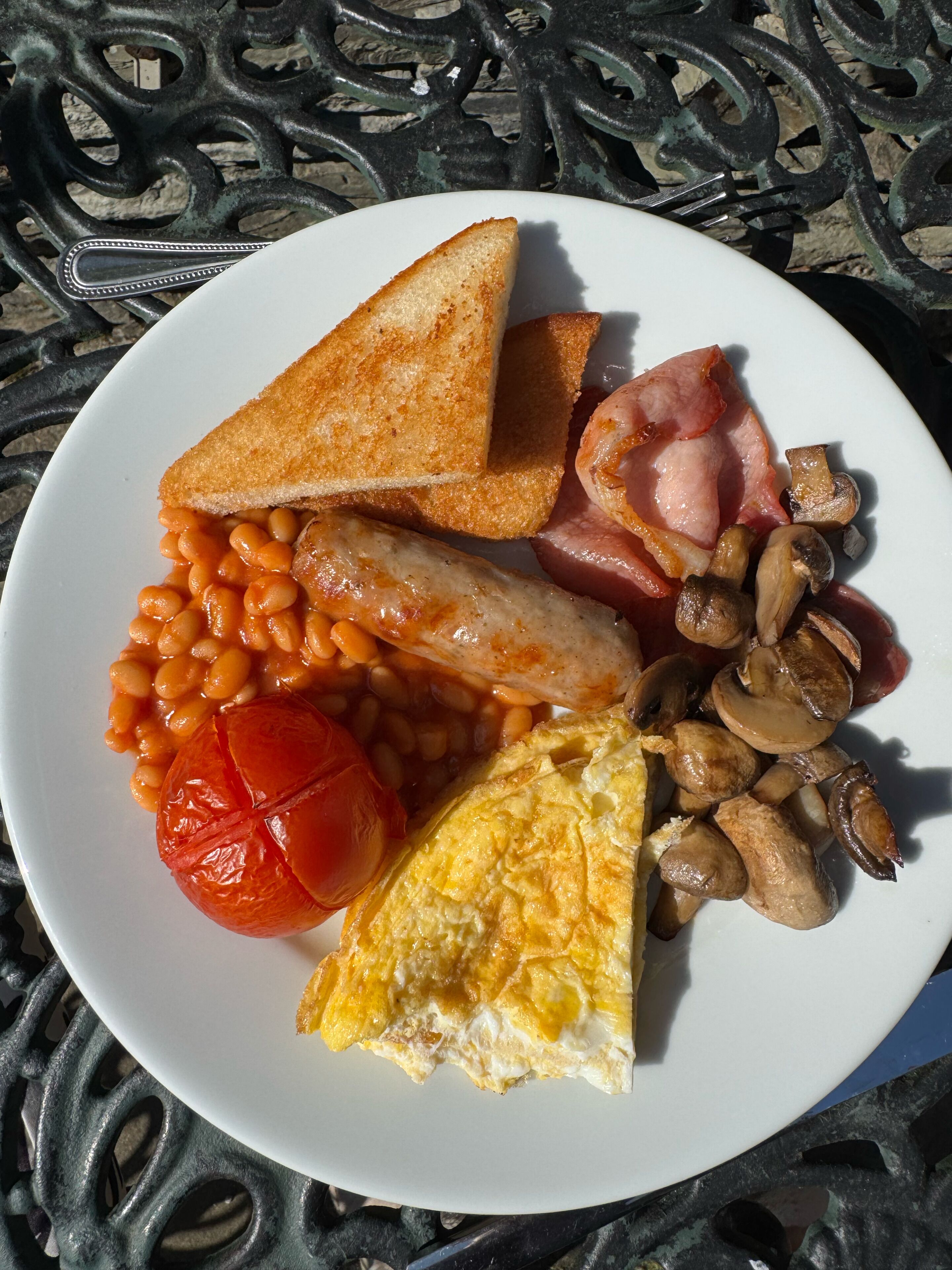 Une assiette de nourriture pour le petit-déjeuner comprenant des toasts, des haricots, des saucisses, des tomates, des champignons et des œufs.