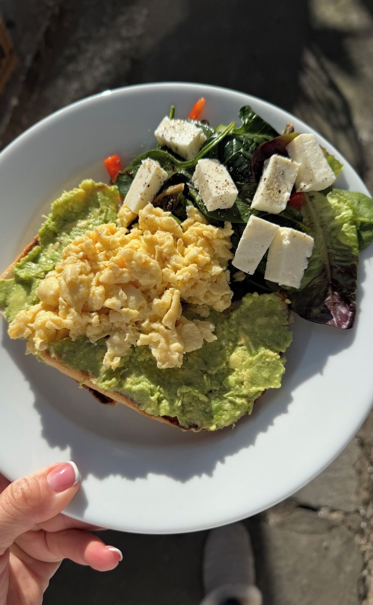 A plate with scrambled eggs, avocado, cheese, and greens.