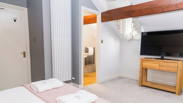 A bedroom with a bed, a TV on a wooden stand, a door, and an open closet. - Denecrest Guest House (Windermere)