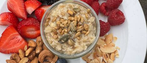 A white plate with a variety of fruits and a bowl of oatmeal with nuts.