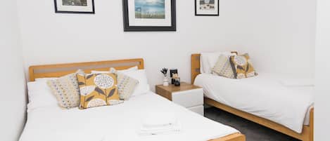 A hotel room with two single beds, a wooden headboard, white bedding, and a small bedside table with a lamp.