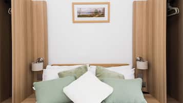 A neatly arranged bedroom with a bed, pillows, bedside lamps, and a framed picture on the wall.