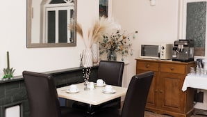 A dining area with a table set for four, a microwave, and a cabinet with kitchen appliances. - Denecrest Guest House (Windermere)