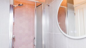 A bathroom with a shower, a toilet, and a round mirror. - Denecrest Guest House (Windermere)