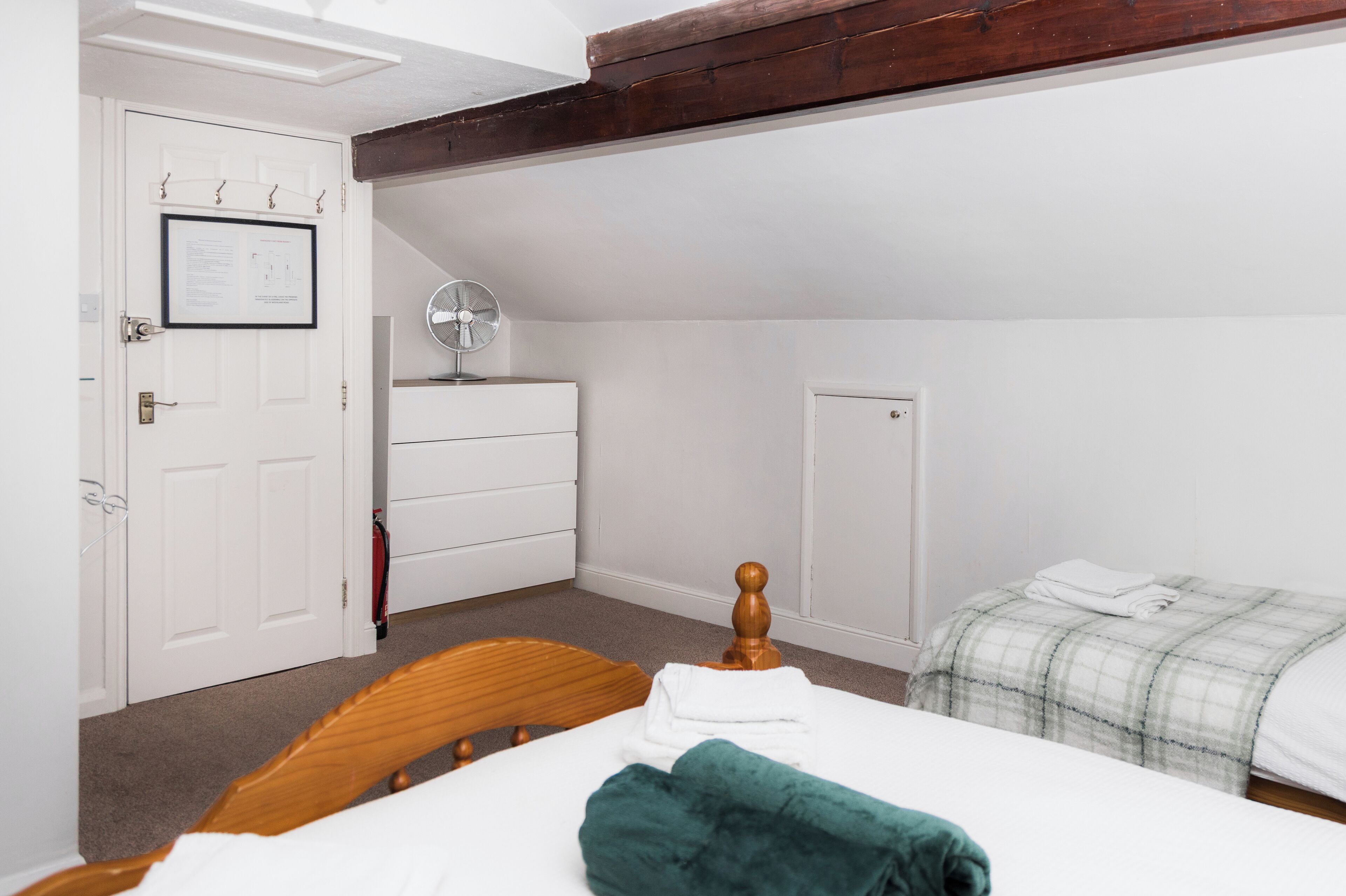 A bedroom with a wooden bed, a white dresser, a white door with a framed notice, and a white ceiling.