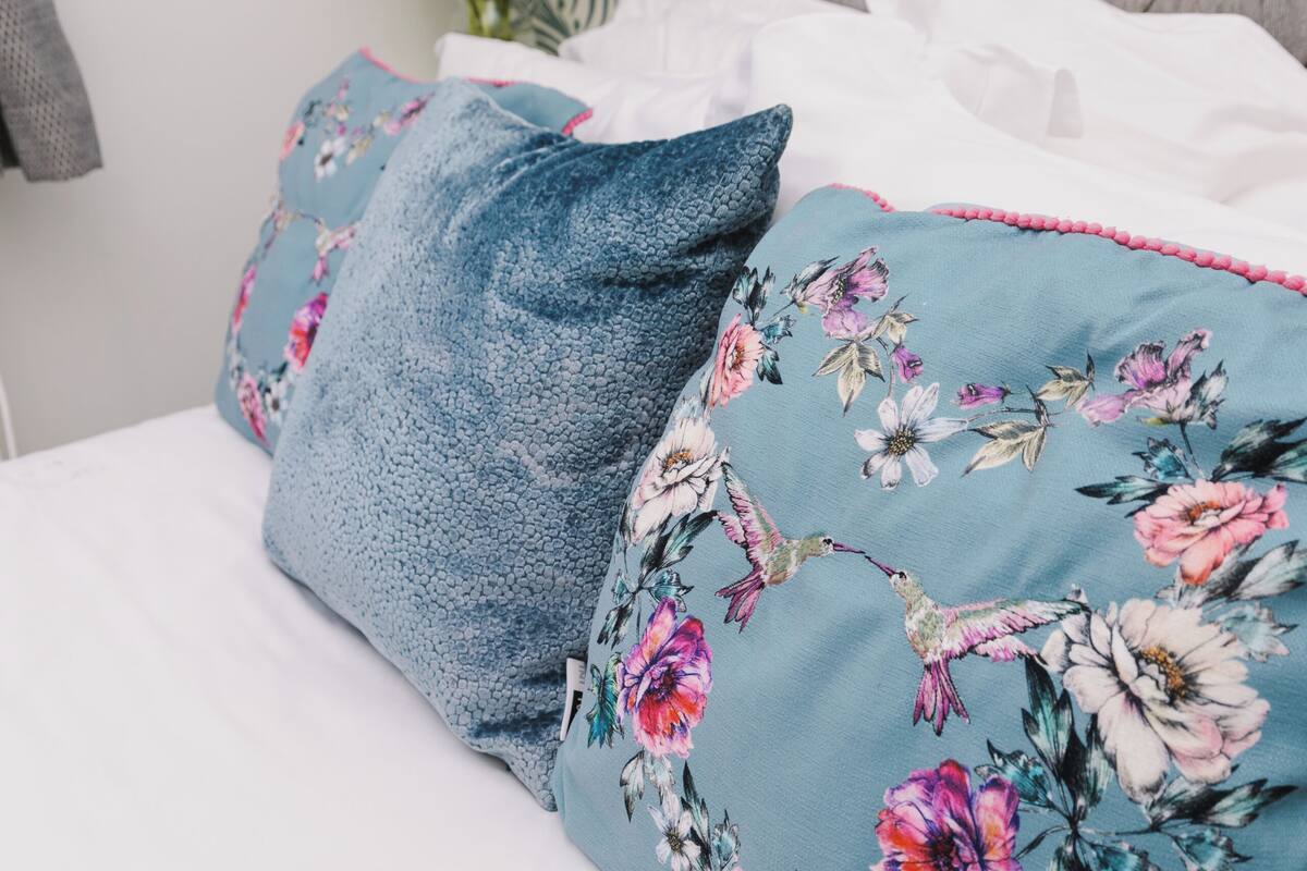 Un letto con cuscini floreali e in denim, una testiera trapuntata e un vaso con fiori.