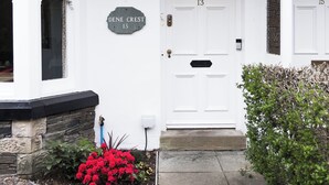 A white building with a stone facade, a black roof, and a door labeled "Dene Crest 13". - Denecrest Guest House (Windermere)