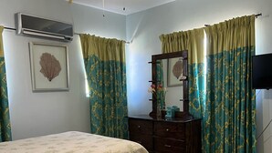 Ein Schlafzimmer mit Bett, Schminktisch, Deckenventilator, Fernseher und gemusterten Vorhängen.