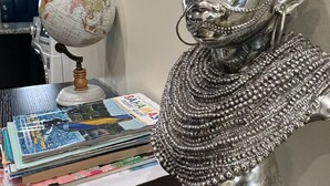 Eine silberne Büstenstatue auf einem Schreibtisch zusammen mit einem Globus und Reisemagazinen.