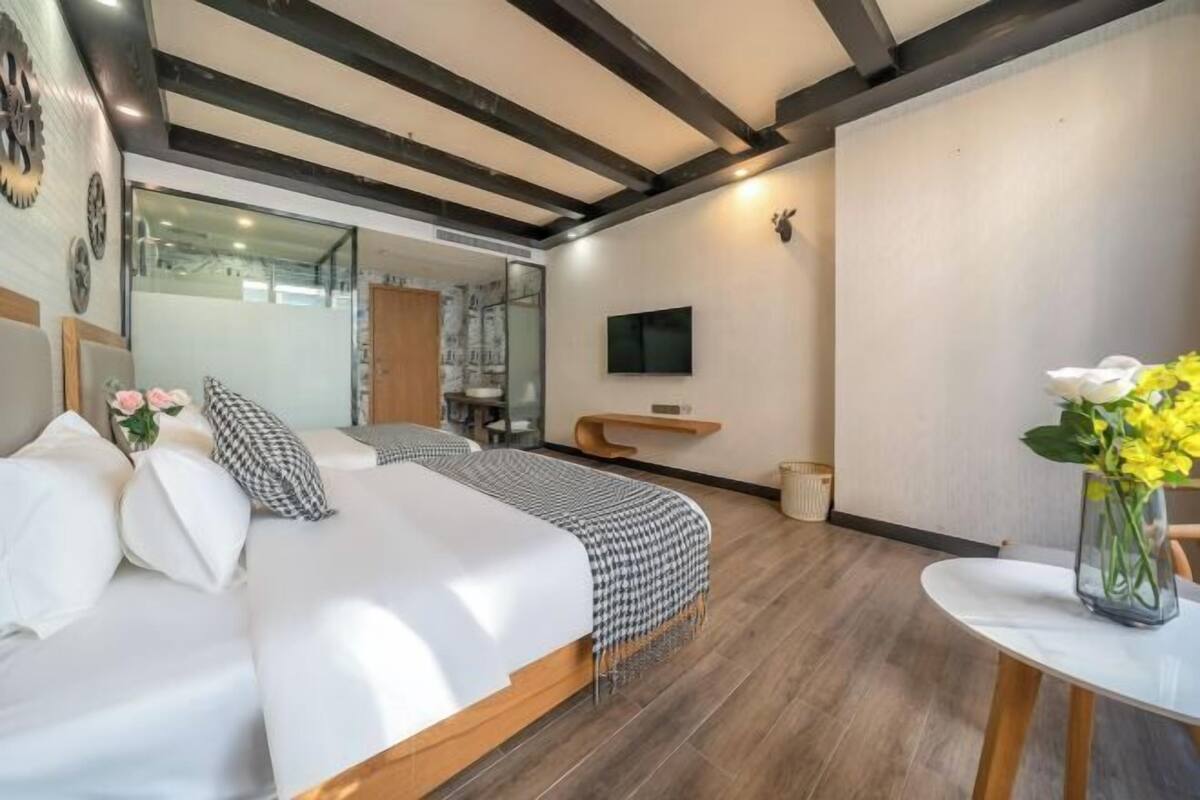A modern hotel room with a large bed, a TV, a small table with a vase, and a wooden ceiling.