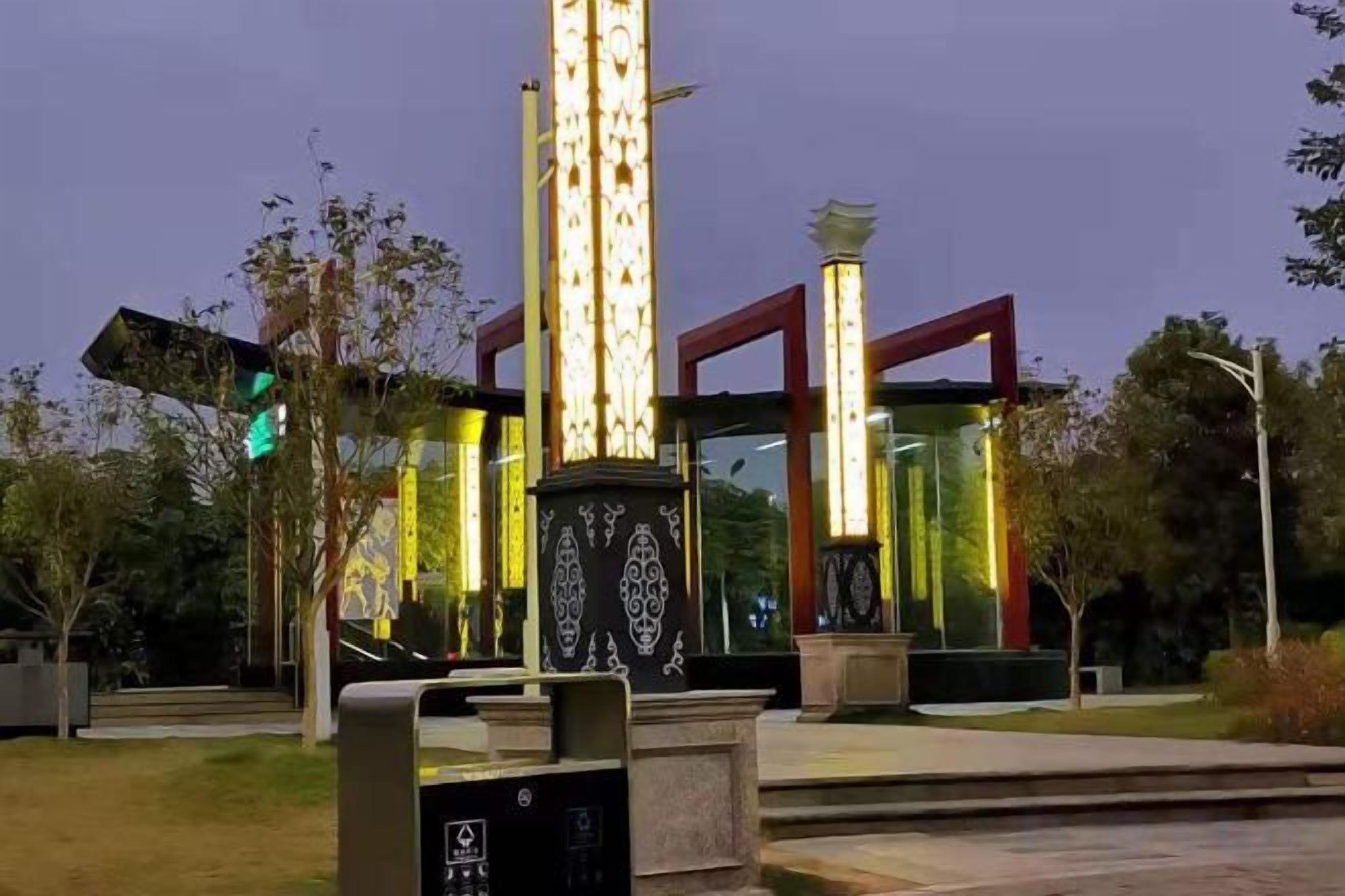 Ett väl upplyst monument med en reflekterande yta, omgivet av ett stenlagt område och träd.