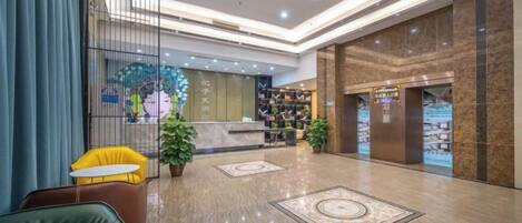 A hotel lobby with a reception desk, seating area, and a large decorative wall.