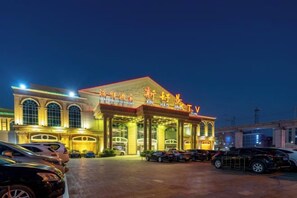 Un hotel con una entrada destacada, varios espacios de estacionamiento y una fachada bien iluminada.