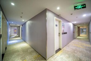 A hotel corridor with a patterned floor, a door with a sign, and a hallway leading to another room.
