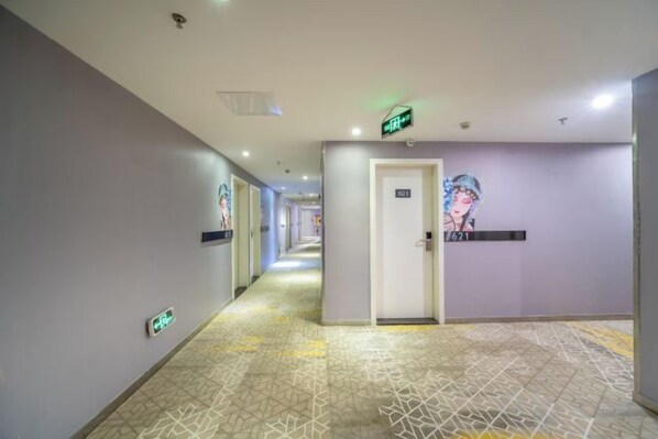 Un pasillo de hotel con piso estampado, una puerta con la etiqueta '02' y una señal de salida verde.