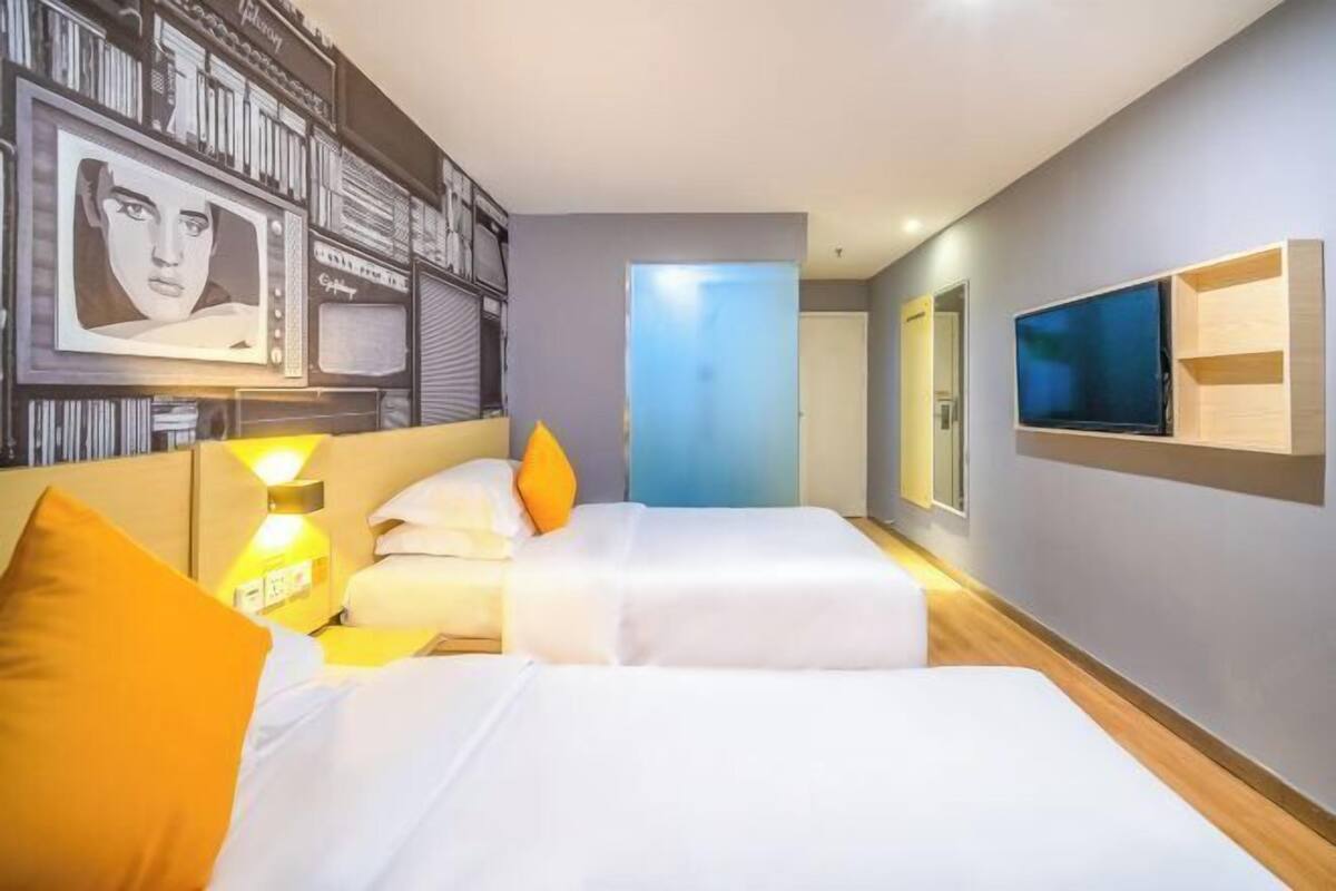 A hotel room with two beds, a TV, a wall-mounted shelf, and a door leading to another room.