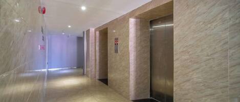 A corridor with marble walls, an elevator, and a fire alarm on the ceiling.