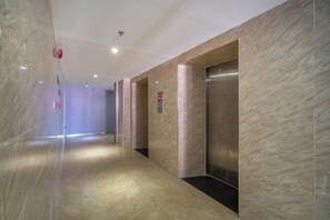 A corridor with marble walls, an elevator, and a fire alarm on the ceiling.