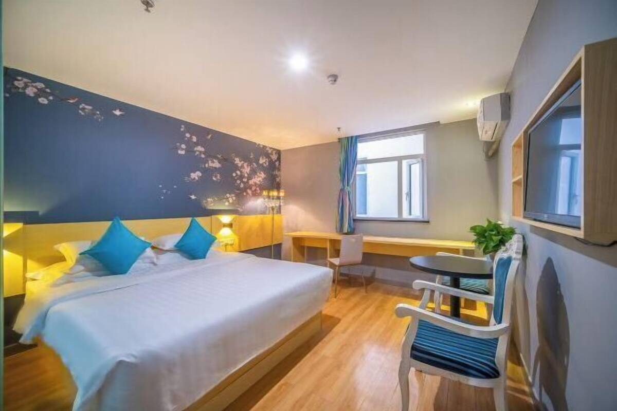 A hotel room with a bed, a desk, a chair, a window, and a wall-mounted TV.