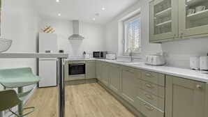 A modern kitchen with a built-in oven, microwave, and toaster. There is a window with blinds, a sink, and a countertop with a bowl and utensils. - Tweedside Retreat - North East Escapes (Berwick-upon-Tweed)