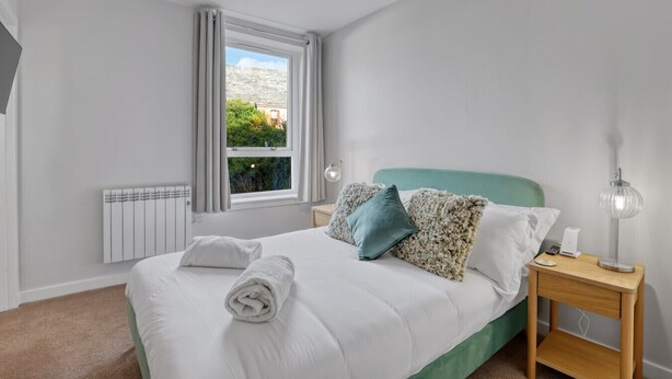 A neatly made bed with pillows, a bedside lamp, and a view of greenery outside the window. - Tweedside Retreat - North East Escapes (Berwick-upon-Tweed)