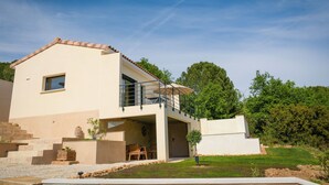 Una casa moderna de dos pisos con techo plano, un balcón y un pequeño patio.