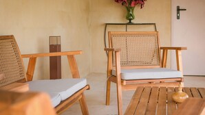 Un rincón de sala de madera con dos sillones y una mesa, un jarrón con flores en un estante, y una puerta con cerradura de llave.