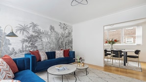 Ein modernes Wohnzimmer mit einem blauen Sofa, einem runden Couchtisch und einem Wandgemälde von tropischen Bäumen.