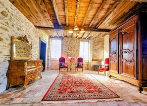 A room with a wooden ceiling, stone walls, a large ornate wooden cabinet, a red patterned rug, and two chairs with floral upholstery. - CHATEAU ARCHE D'AURE (Vicq-d'Auribat)