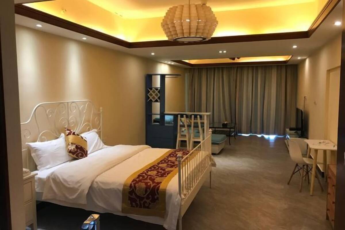 Una habitación de hotel con cama, escritorio, silla, televisor y cortina.