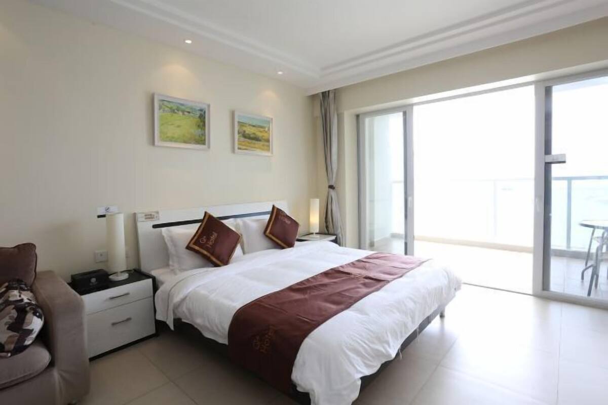 Habitación de hotel con una cama grande, una mesita de noche, una silla y un balcón con vistas.