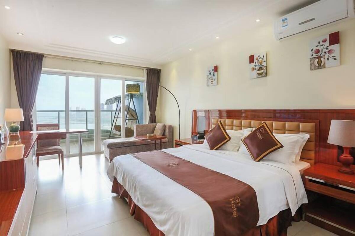 Habitación de hotel con una cama grande, un escritorio, una silla, un balcón con vistas y obras de arte en las paredes.