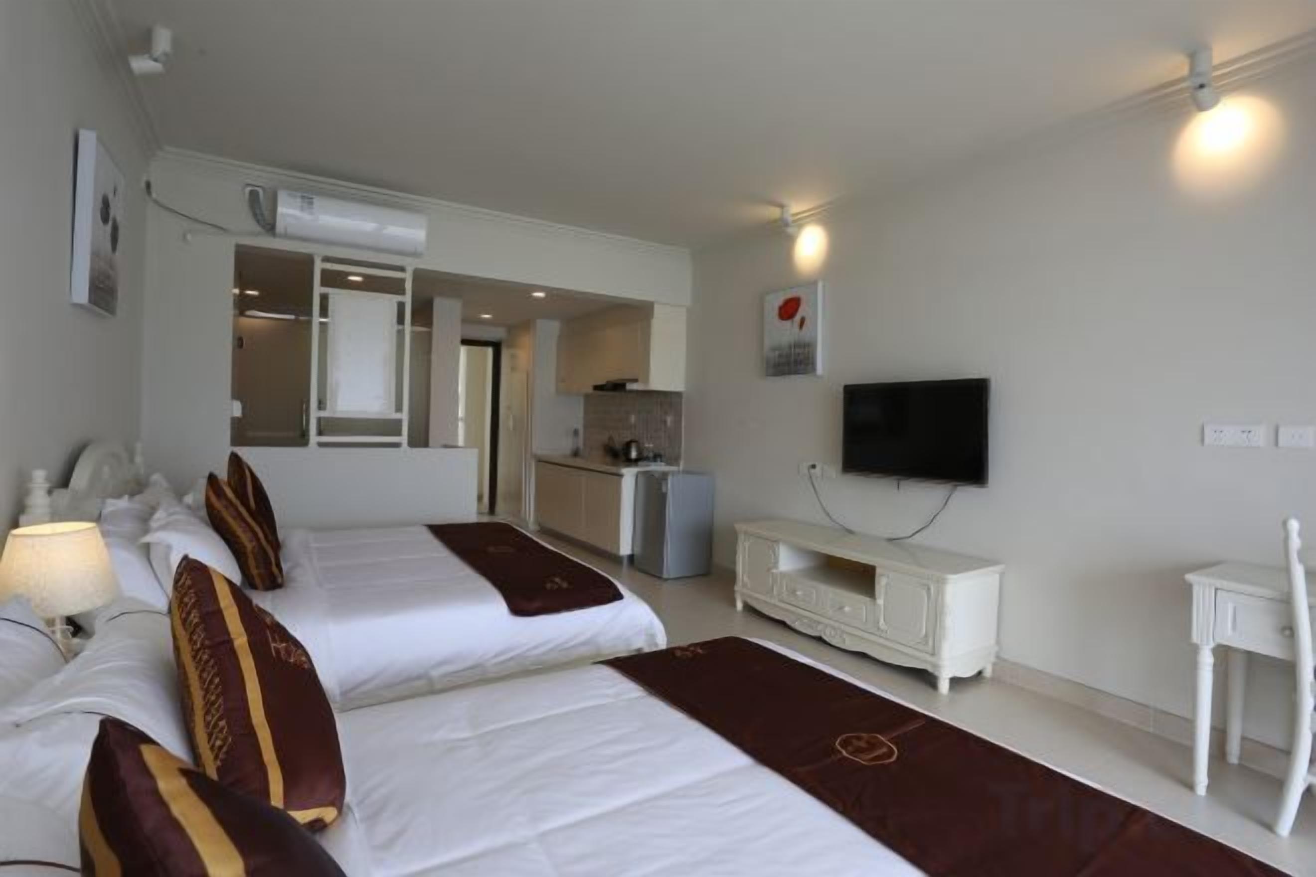 Hotellihuone, jossa on kaksi sänkyä, televisio, pieni keittiö ja kylpyhuone.
