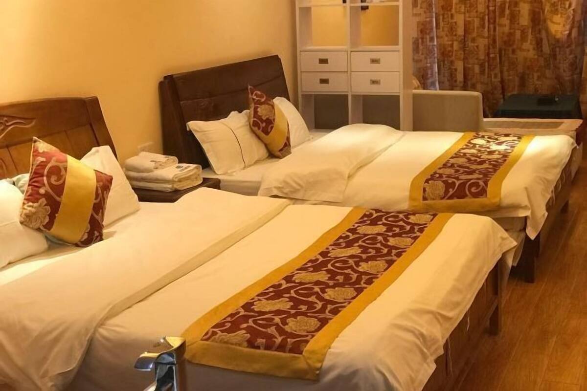 Dos camas individuales con sábanas blancas y almohadas decorativas, un cabecero de madera, una mesita de noche pequeña y un armario con varios cajones.