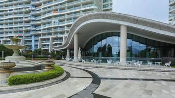 A modern hotel with a curved facade, outdoor seating area, and a central fountain.