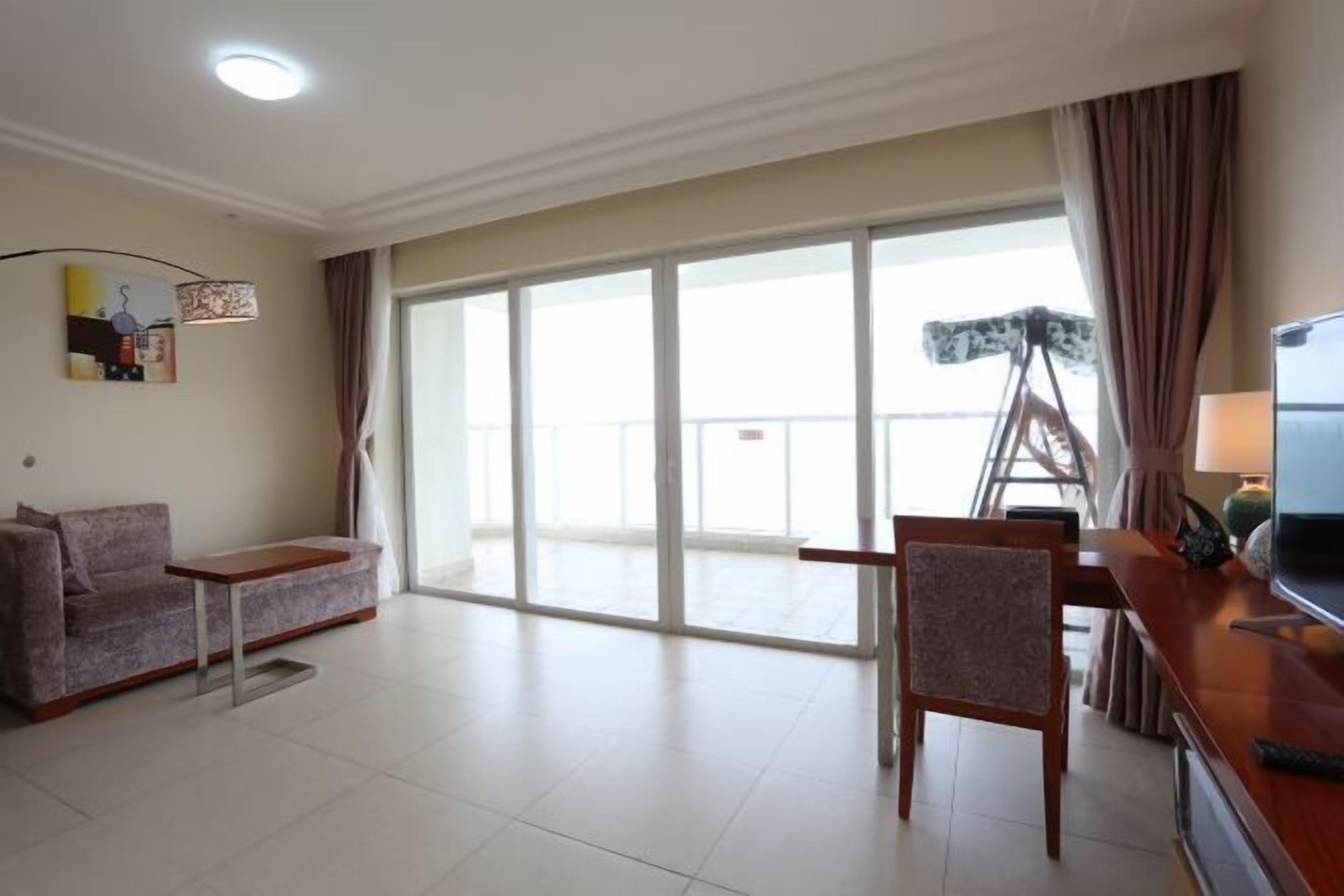 A living room with a sofa, a dining table, a chair, a TV, and a large sliding glass door leading to a balcony.