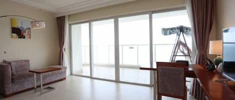 A living room with a sofa, a dining table, a chair, a TV, and a large sliding glass door leading to a balcony.