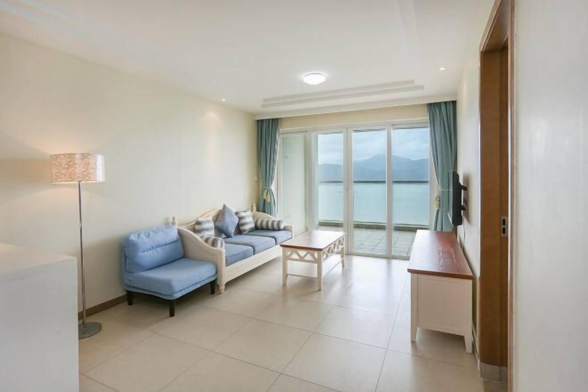 Habitación de hotel moderna con sofá, una mesita, una lámpara y vistas al mar a través de amplias ventanas.